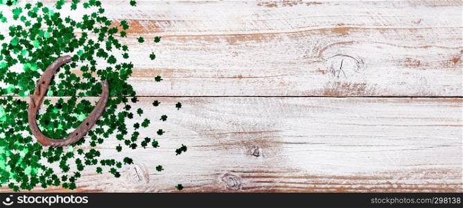Bright green shamrock and rusty horseshoe for Saint Patrick Day on white rustic wooden background