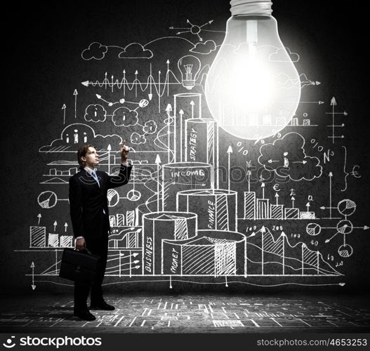 Bright idea. Businessman pointing at light bulb with business sketches at background