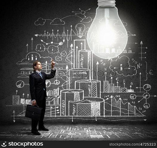 Bright idea. Businessman pointing at light bulb with business sketches at background