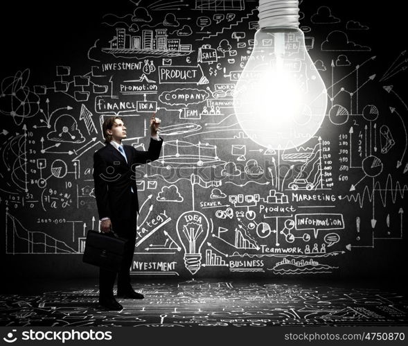 Bright idea. Businessman pointing at light bulb with business sketches at background