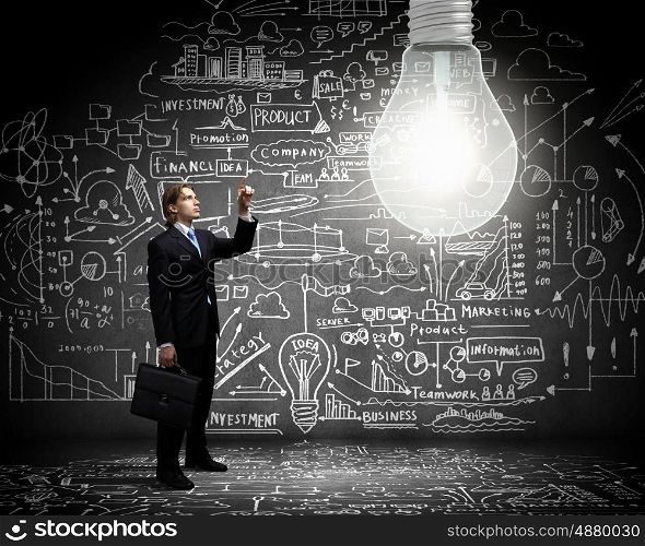 Bright idea. Businessman pointing at light bulb with business sketches at background