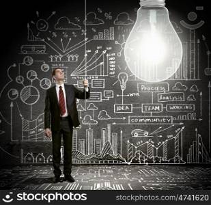 Bright idea. Businessman switching on light bulb with business sketches at background