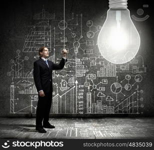 Bright idea. Businessman switching on light bulb with business sketches at background