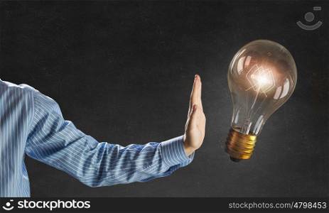 Bright idea in hand. Businessman hand showing stop gesture and glass glowing light bulb on dark background