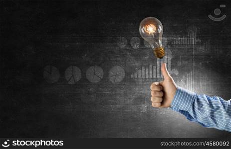 Bright idea in hand. Businessman hand showing thumb up and glass glowing light bulb on dark background