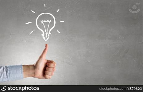 Bright idea in hand. Businessman hand showing thumb up and idea light bulb concept on concrete background