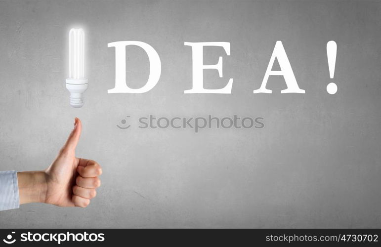 Bright idea in hand. Businessman hand showing thumb up and idea light bulb concept on concrete background