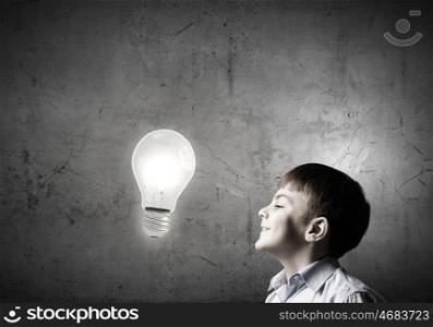 Bright idea. Young boy of school age looking up at light bulb