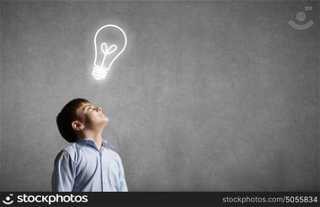 Bright idea. Young boy of school age looking up at light bulb