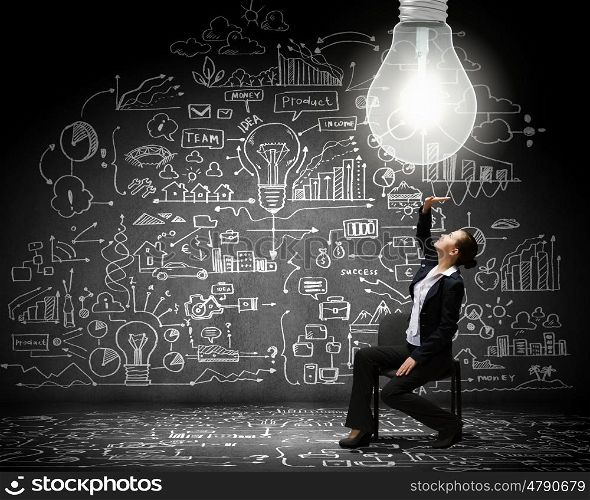 Bright idea. Young businesswoman sitting on chair with business sketches at background