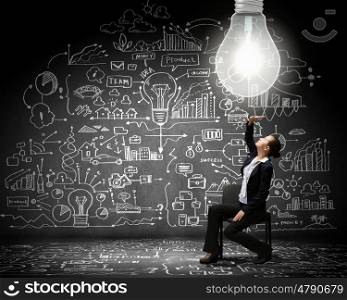 Bright idea. Young businesswoman sitting on chair with business sketches at background