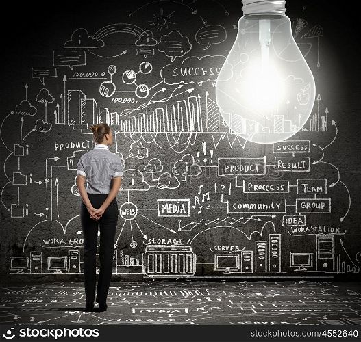 Bright idea. Young businesswoman with bulb and business sketches at background