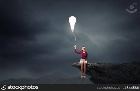 Bright idea. Young pretty woman sitting on rock edge with bulb balloon in hand