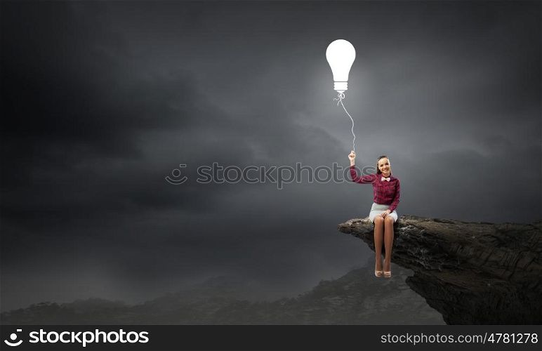 Bright idea. Young pretty woman sitting on rock edge with bulb balloon in hand
