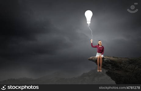 Bright idea. Young pretty woman sitting on rock edge with bulb balloon in hand