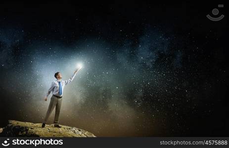 Bright light of education in darkness. Young screaming businessman on pile reaching hand with opened book