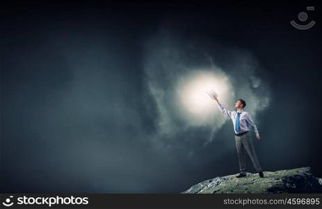 Bright light of education in darkness. Young screaming businessman on pile reaching hand with opened book