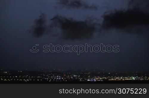 Bright lightnings in dark sky over illuminated city. Night storm