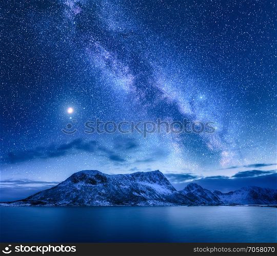 Bright Milky Way over snow covered mountains and sea at night in winter in Norway. Landscape with snowy rocks, starry sky, reflection in water, fjord. Lofoten Islands. Space. Beautiful milky way