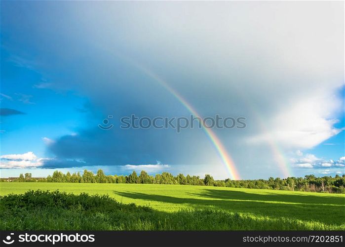 Bright multi-colored rainbow over the green field on the background of a large cloud.