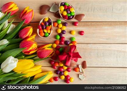 Bright multi-colored tulips and chocolate Easter eggs on a wooden background. Festive design, place for text.. Multi-colored Tulips and Chocolate Easter Eggs