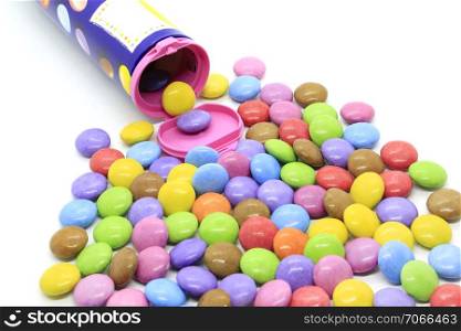 Bright multicolored glazed chocolate candies out of the container on a white background