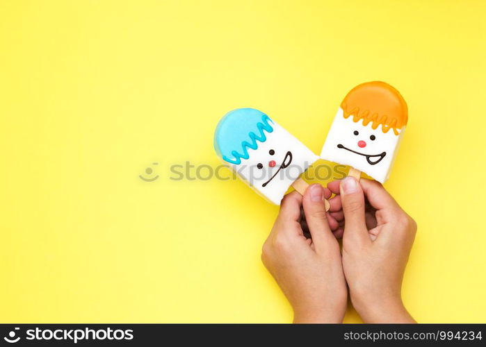 bright multicolored souffle dessert in white chocolate on a stick in hand with a smiley face on a yellow background dessert candies selective focus.. bright multicolored souffle dessert in white chocolate on a stick in hand with a smiley face on a yellow background dessert candies selective focus