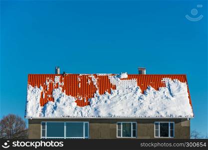 Bright orange roof covered with snow on blue sky background.