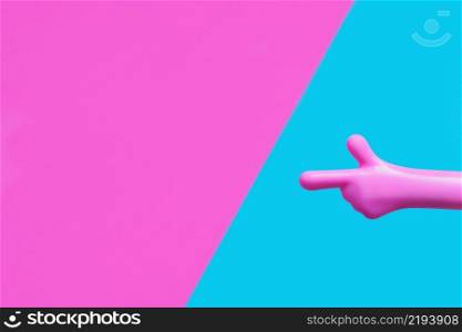 bright pink plastic hand pointing with index finger at pink-blue background. copy space.