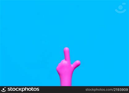 bright pink plastic hand pointing with index finger on a blue background. copy space.
