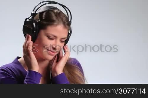 Bright positive teenage girl holding her headphones with both hand and enjoying the sound of music on white. Attractive young woman having fun, flirting with camera playfully, making seductive looks while listening to the music in earphones.