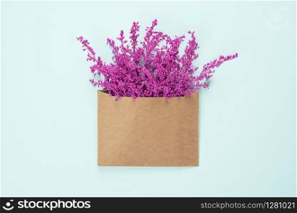 Bright purple or violet flowers in craft brown envelope with copy space isolated on light blue background. Trendy banner for Valentines Day or International Womens Day .. Bright purple or violet flowers in craft brown envelope with copy space isolated on light blue background.