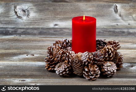 Bright red candle inside of real pine cone wreath for the Christmas season on rustic wooden boards