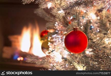 Bright red Christmas ornament hanging on silver Xmas Tree with fire place in background