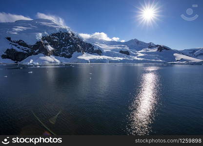 Bright sun and cloudless sky over mountain with snow and ice by the sea in Antarctica