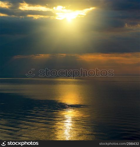 Bright sun in black clouds over ocean with sun track.