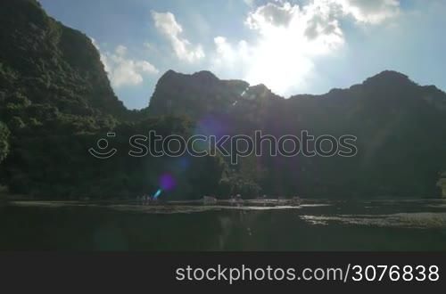 Bright sun shining over the green islets and water with touristic boat having nature excursions. Traveling in Ha Long Bay, Vietnam