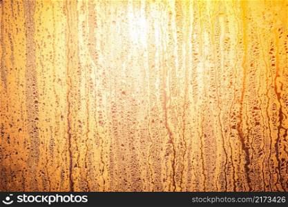 Bright sun shinning through the glass window. Sunrise in yellow orange tawny tints. The drops of water on the glass surface. Ideal background for the illustrations and collages.. Bright sun shinning through the glass window