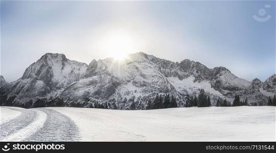 Bright winter landscape with snow-capped Alps mountain peaks, snow-covered nature, and snowy alpine road, on a sunny day, near Ehrwald, Austria.