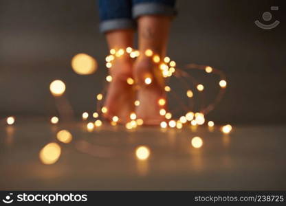 Bright yellow garlands around female feet on the floor on a dark background with a copy space. Can be used for display or montage your ideas. Christmas composition of female feet with garlands on the floor around a dark background with a copy space