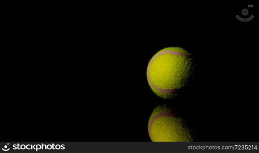 Bright Yellow Tennis Ball on dark mirror with reflections on a black background
