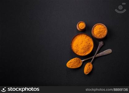 Bright yellow turmeric or curry spice for Asian food preparation on dark concrete background