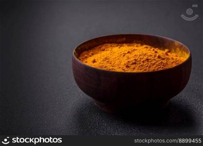 Bright yellow turmeric or curry spice for Asian food preparation on dark concrete background