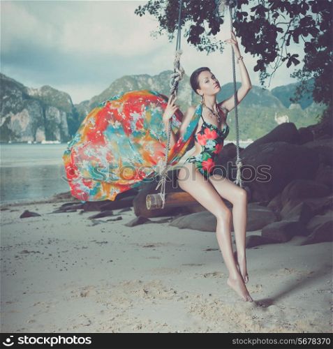Bright young lady on the beach a swing
