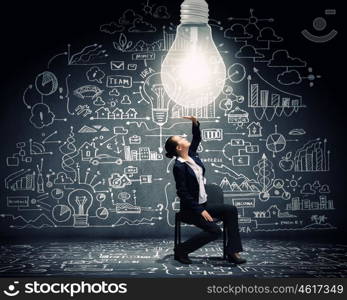 Brilliant idea. Young businesswoman sitting on chair with big light bulb above