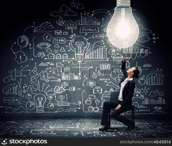 Brilliant idea. Young businesswoman sitting on chair with big light bulb above