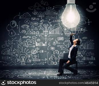 Brilliant idea. Young businesswoman sitting on chair with big light bulb above
