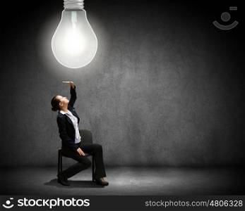 Brilliant idea. Young businesswoman sitting on chair with big light bulb above