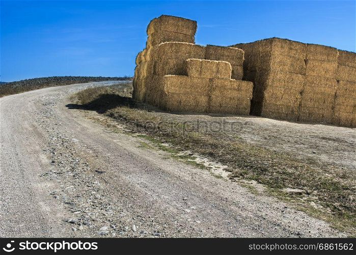 Briquettes of wheat hay near the dirt road in Italy. Plowed sloping hills of Tuscany in the autumn. Rural landscape with field after harvest.