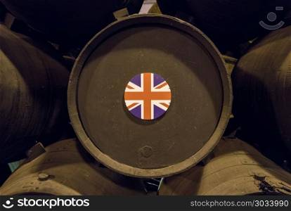 British flag on wooden wine barrels for sherry aging. UK Union Jack flag on stacked oak casks or barrels along wall of winery for aging sherry or port. British flag on wooden wine barrels for sherry aging